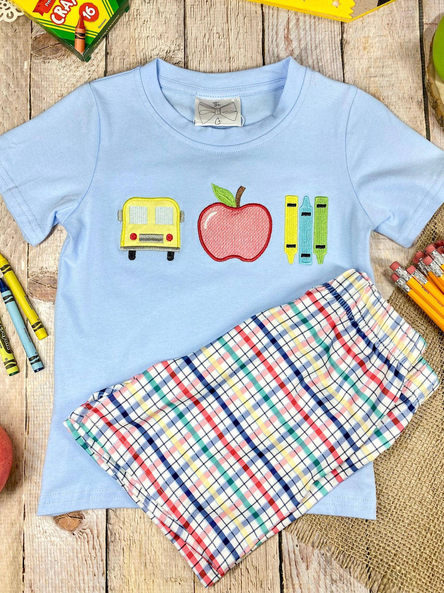 Children's outfit with light blue shirt and plaid shorts on a wooden background