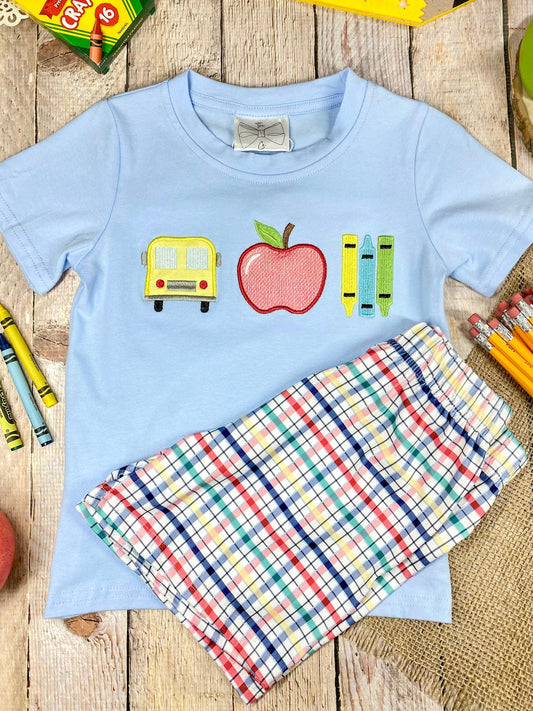 Children's outfit with light blue shirt and plaid shorts on a wooden background