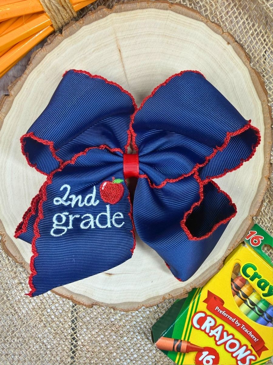 Blue and red bow with '2nd grade' text on a wooden surface with Crayola crayons.