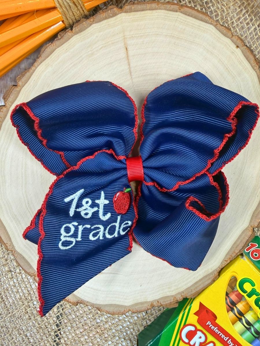 Blue and red bow with '1st grade' text and apple emblem on a wooden surface.