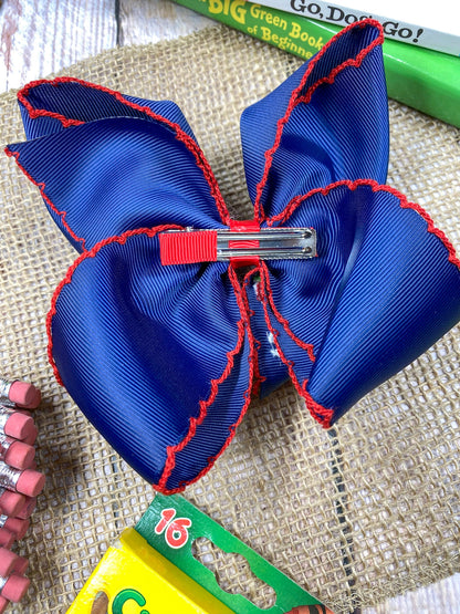 Blue and red bow hair clip on a textured surface with books in the background
