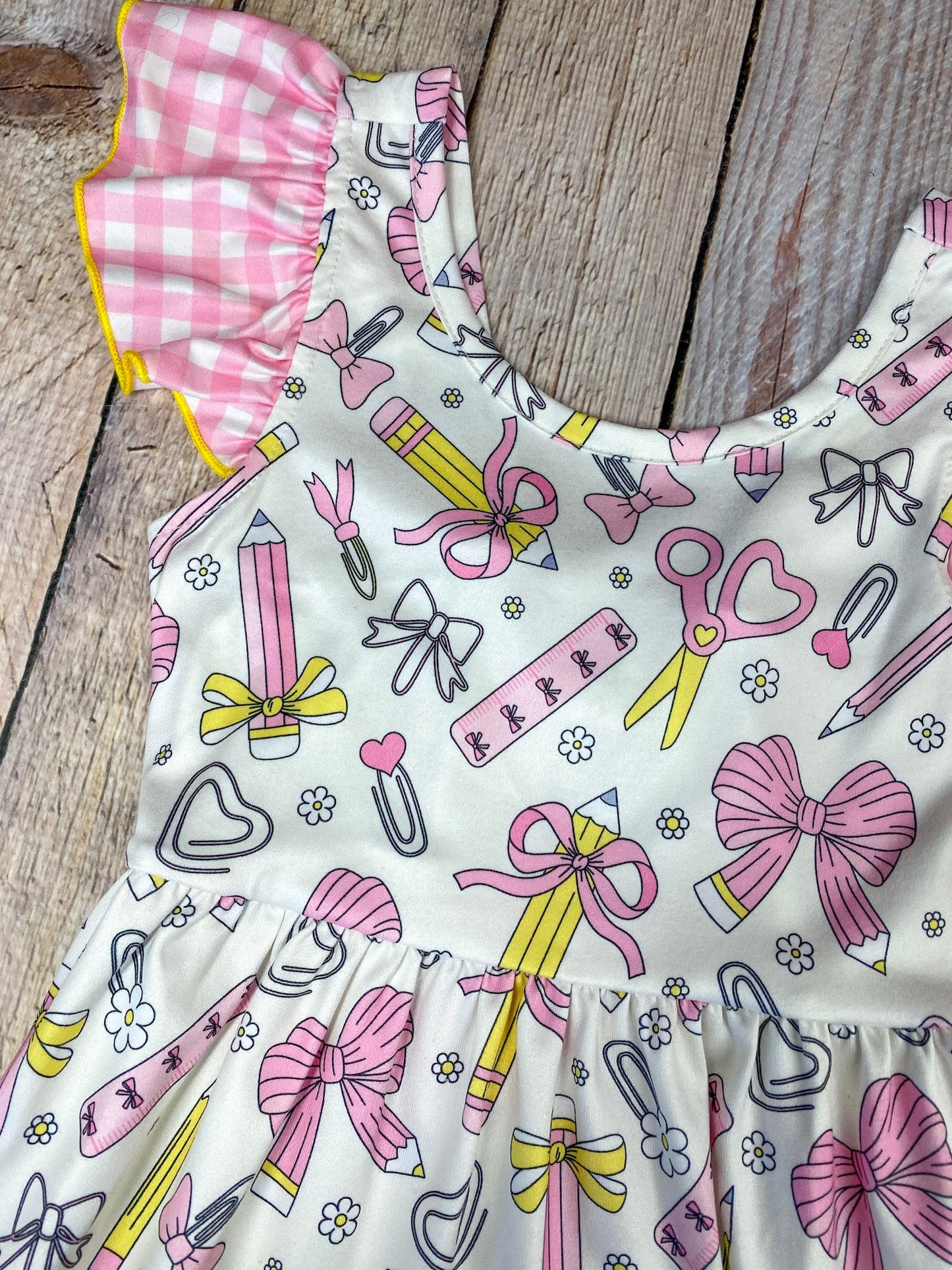 Children's dress with stationery-themed print on a wooden background