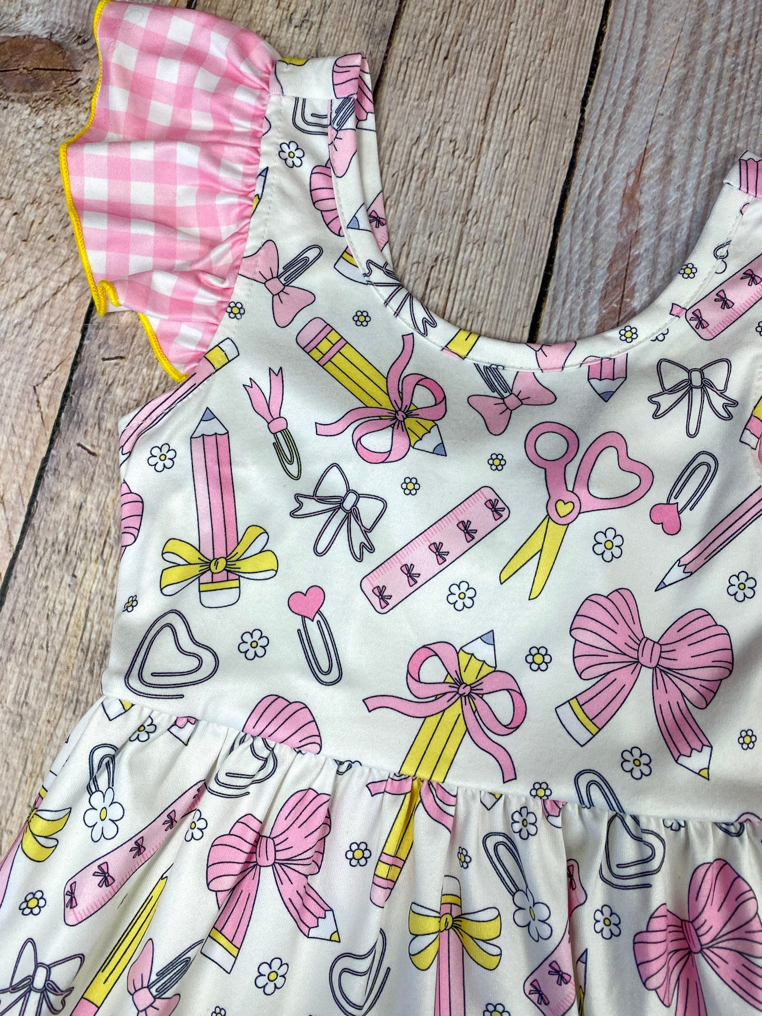 Children's dress with stationery-themed print on a wooden background