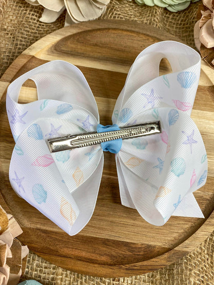 Large white hair bow with seashell patterns on a wooden surface