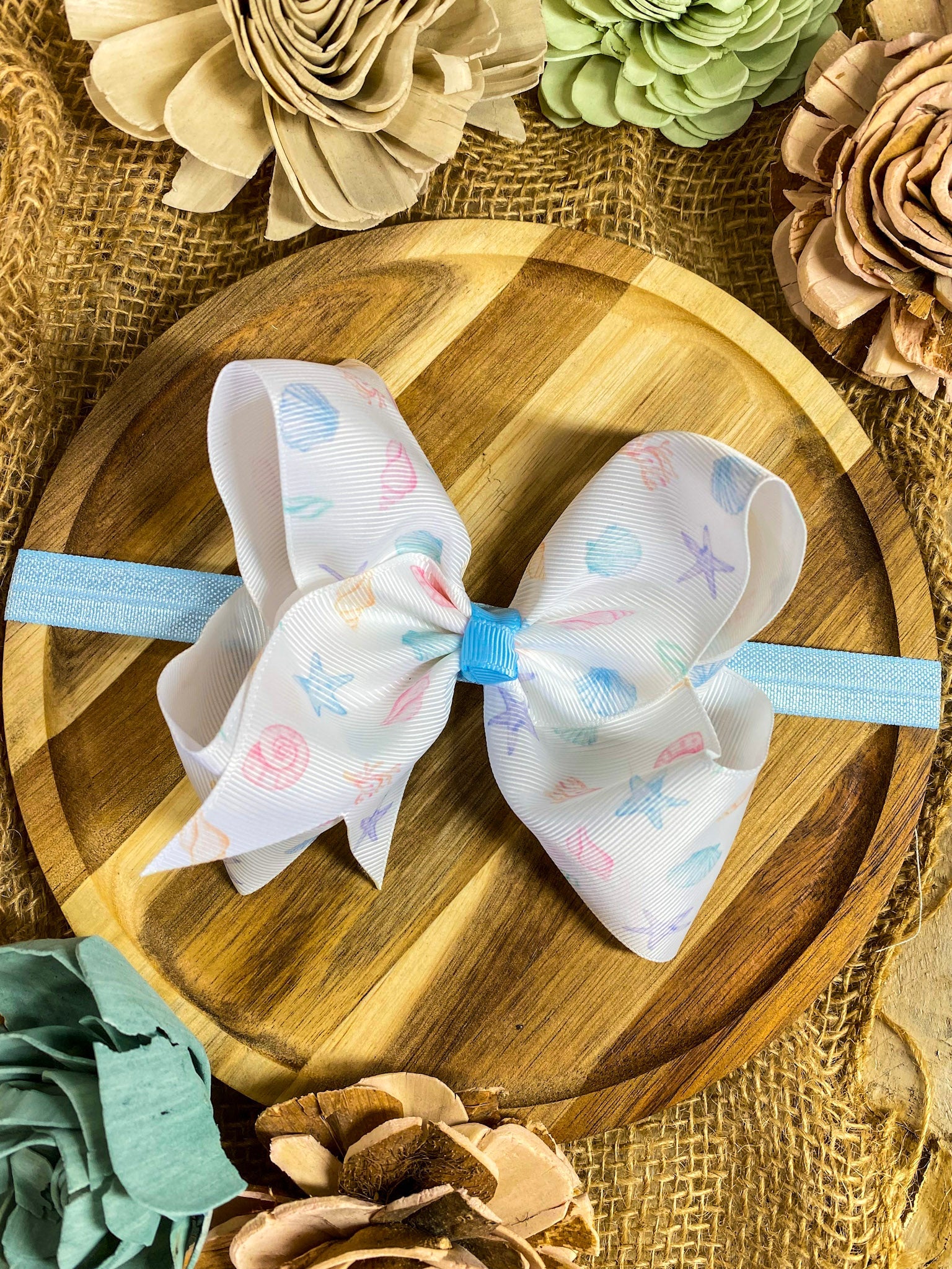 Large seashell bow with a blue headband on a wood
