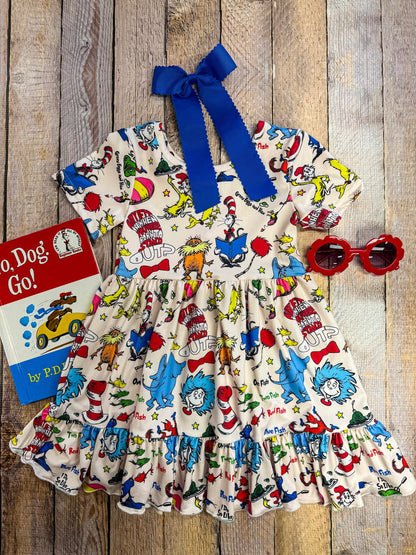 Children's dress with colorful print and blue bow on a wooden surface, accompanied by a book titled 'Dr. Seuss' book'.