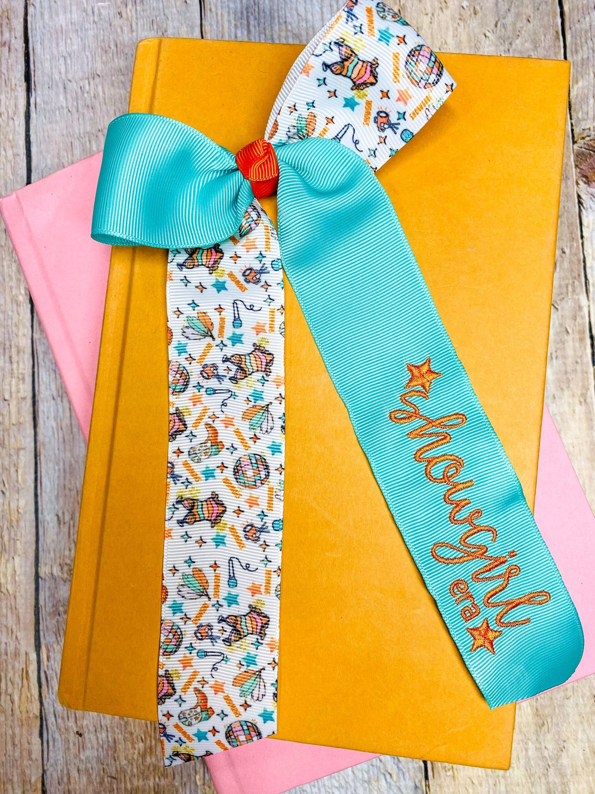 Showgirl Era long ribbon hair bow with colorful print on a wooden surface