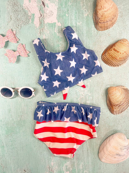 A bikini set with a star patterned top and striped bottom, along with sunglasses and seashells on a blue background.