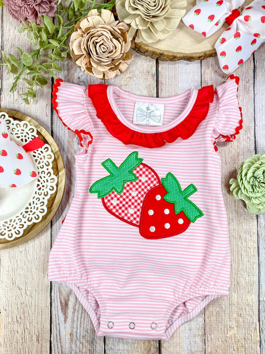 Pink and red striped baby romper with strawberry design on a wooden background