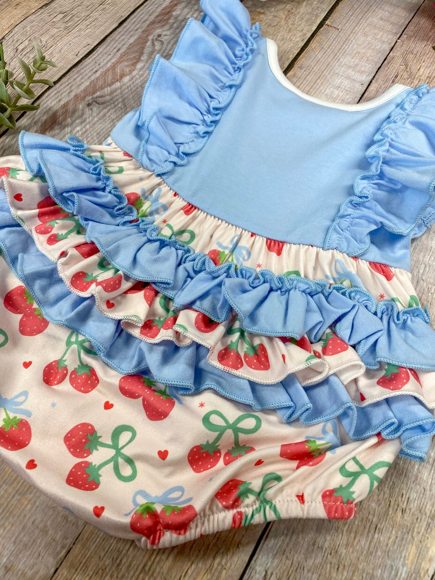 Baby romper with blue ruffled sleeves and cherry pattern on a wooden background