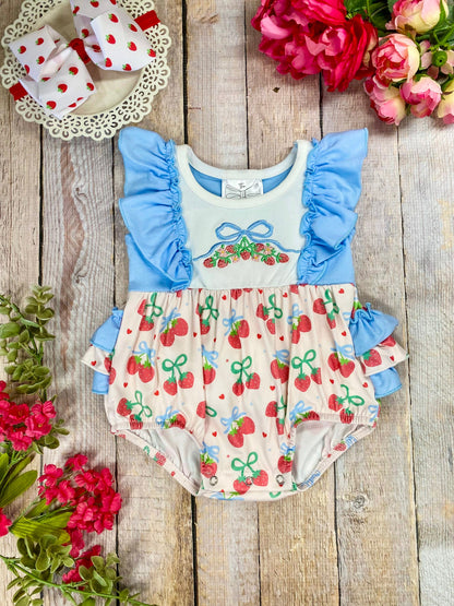 Baby romper with blue ruffled sleeves and cherry pattern on a wooden background