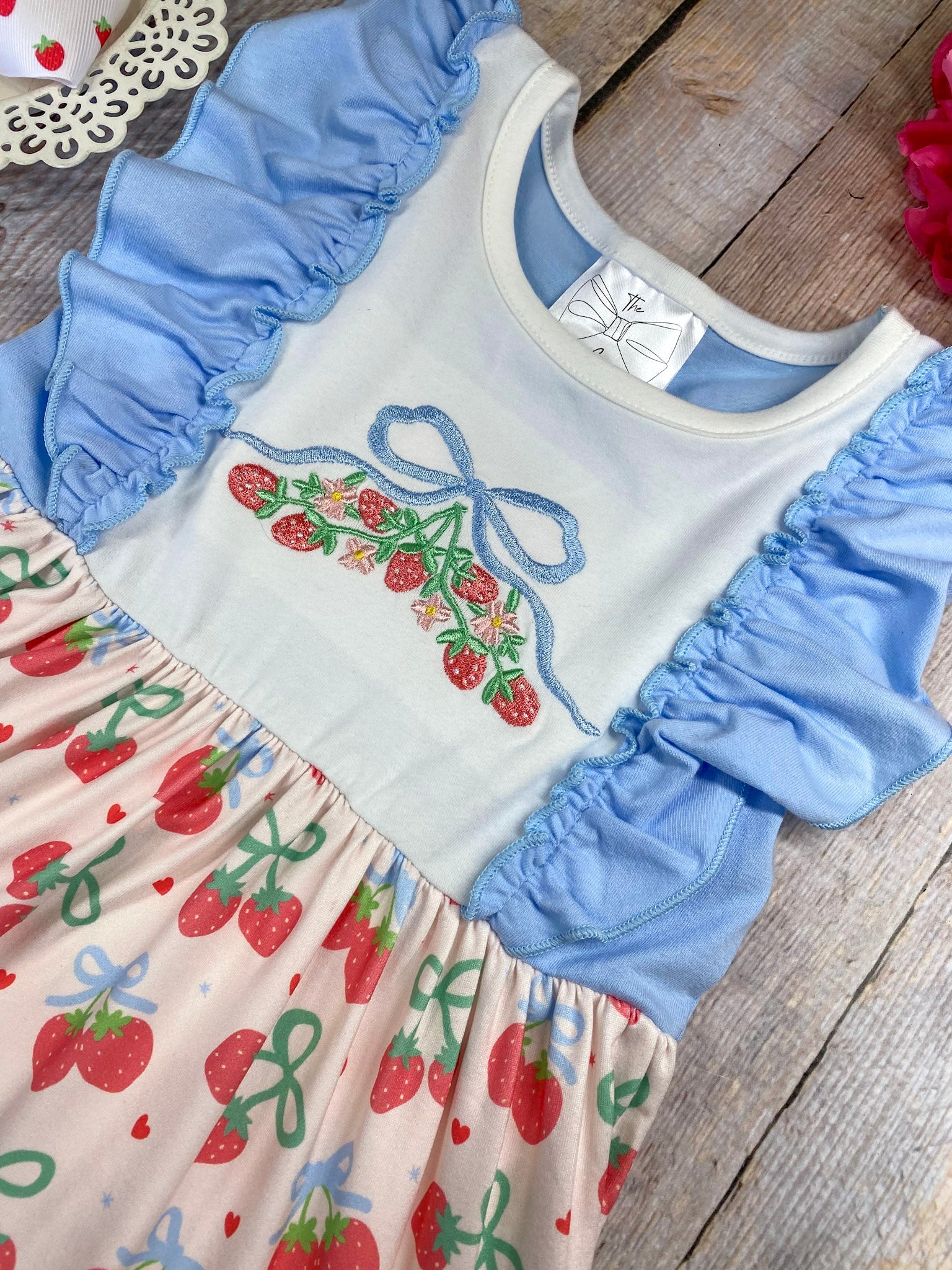 Children's dress with cherry pattern and blue ruffles on a wooden background