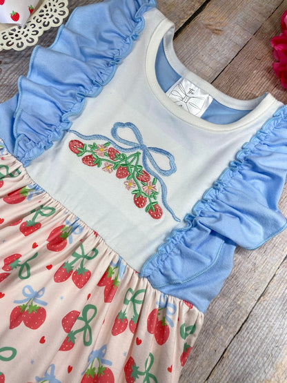 Children's dress with cherry pattern and blue ruffles on a wooden background