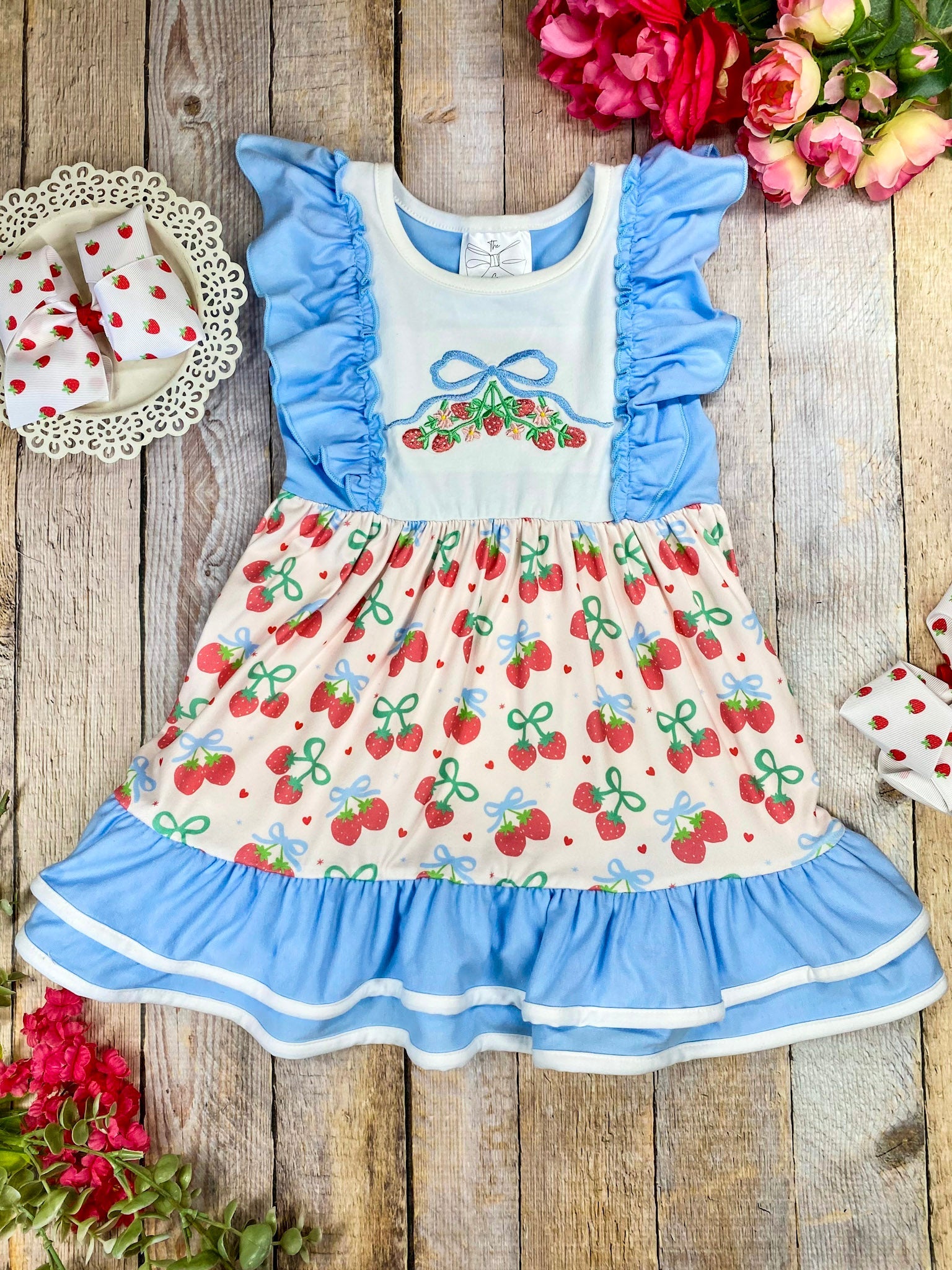 Children's dress with cherry pattern and blue ruffles on a wooden background