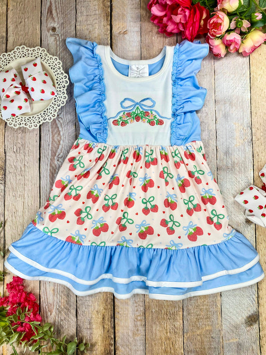 Children's dress with cherry pattern and blue ruffles on a wooden background