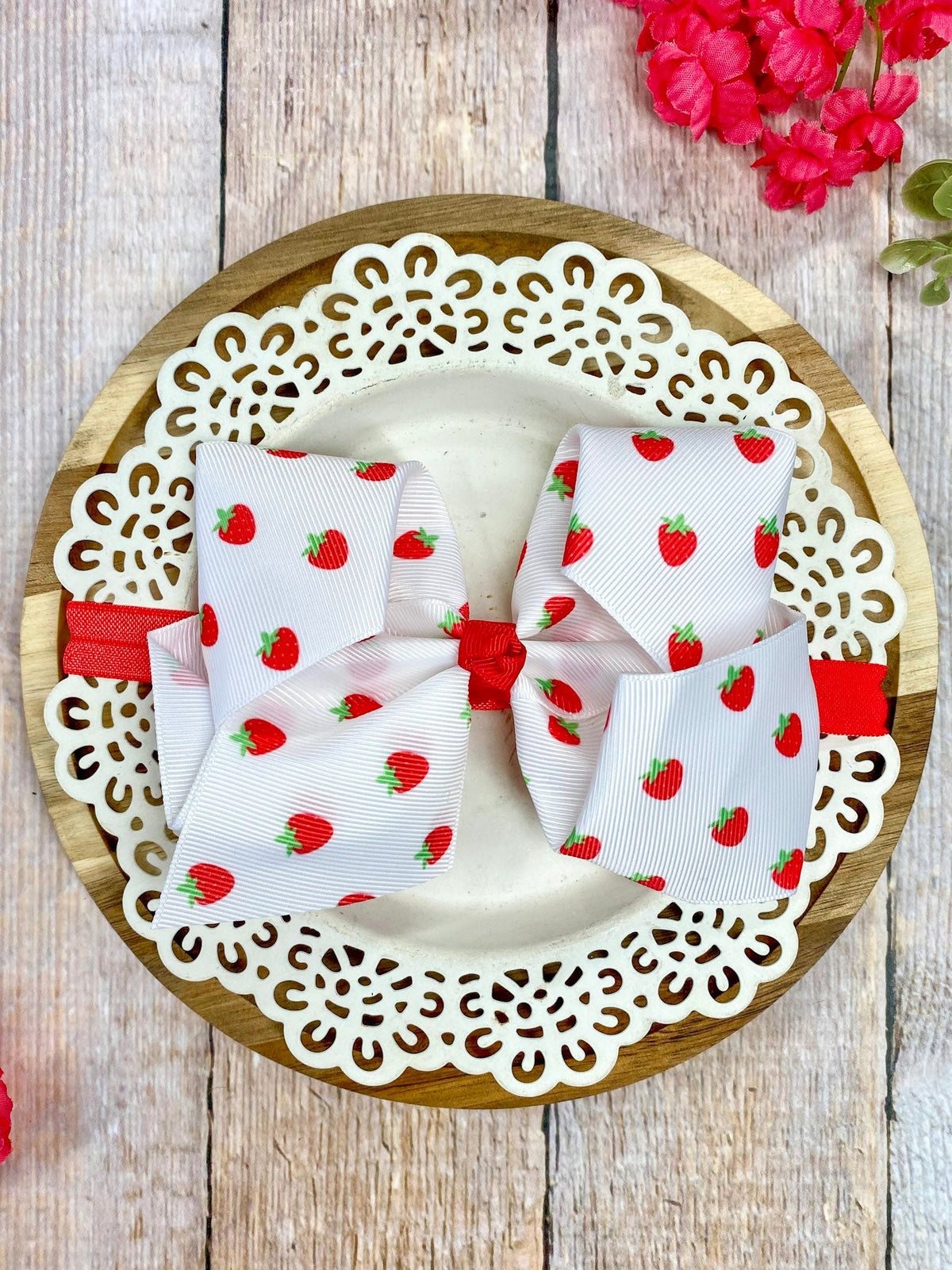 White strawberry print hair bow on a wooden plate with lace edge