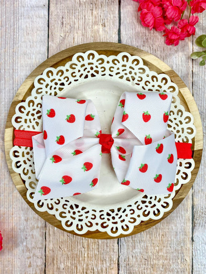 White strawberry print hair bow on a wooden plate with lace edge