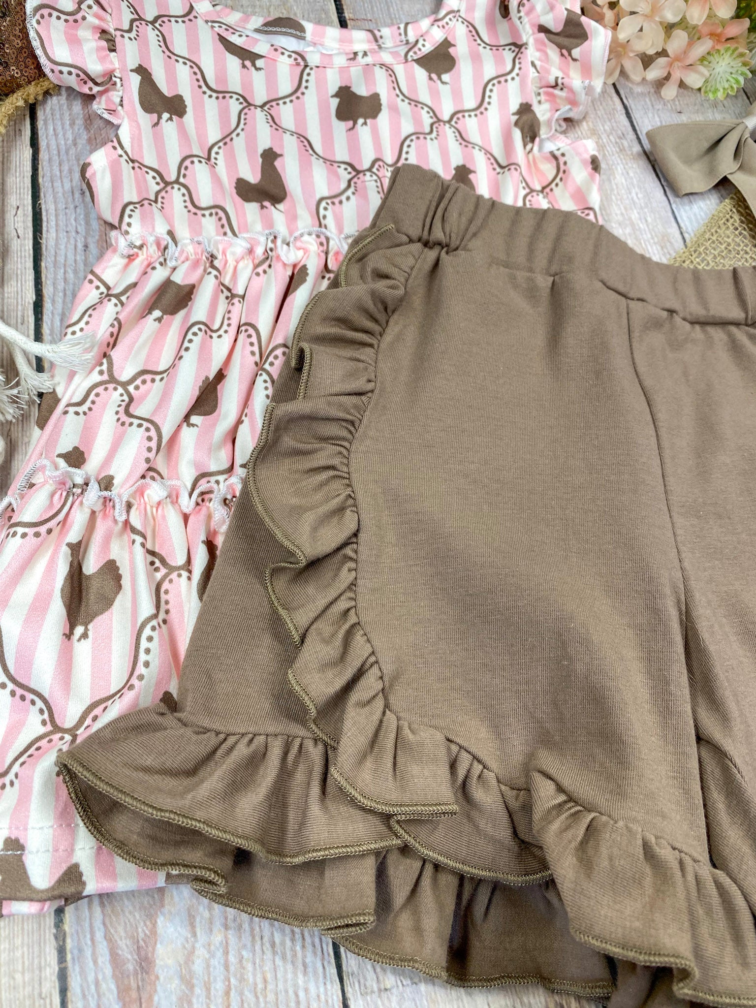 Pink ruffled top with chicken pattern and brown shorts on a wooden background