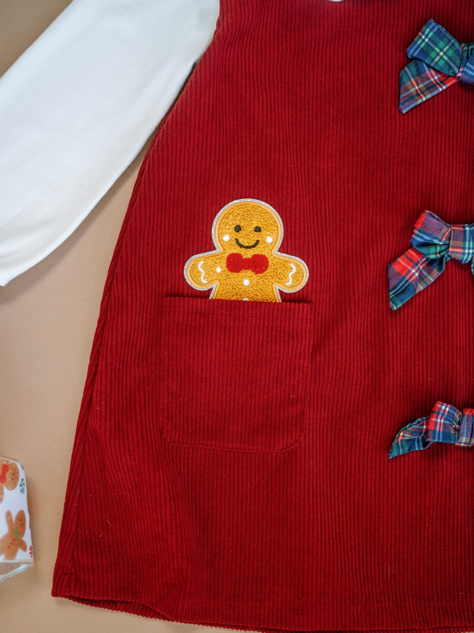 Red corduroy dress with a gingerbread man design and plaid bows on a beige surface.