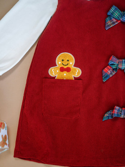Red corduroy dress with a gingerbread man design and plaid bows on a beige surface.