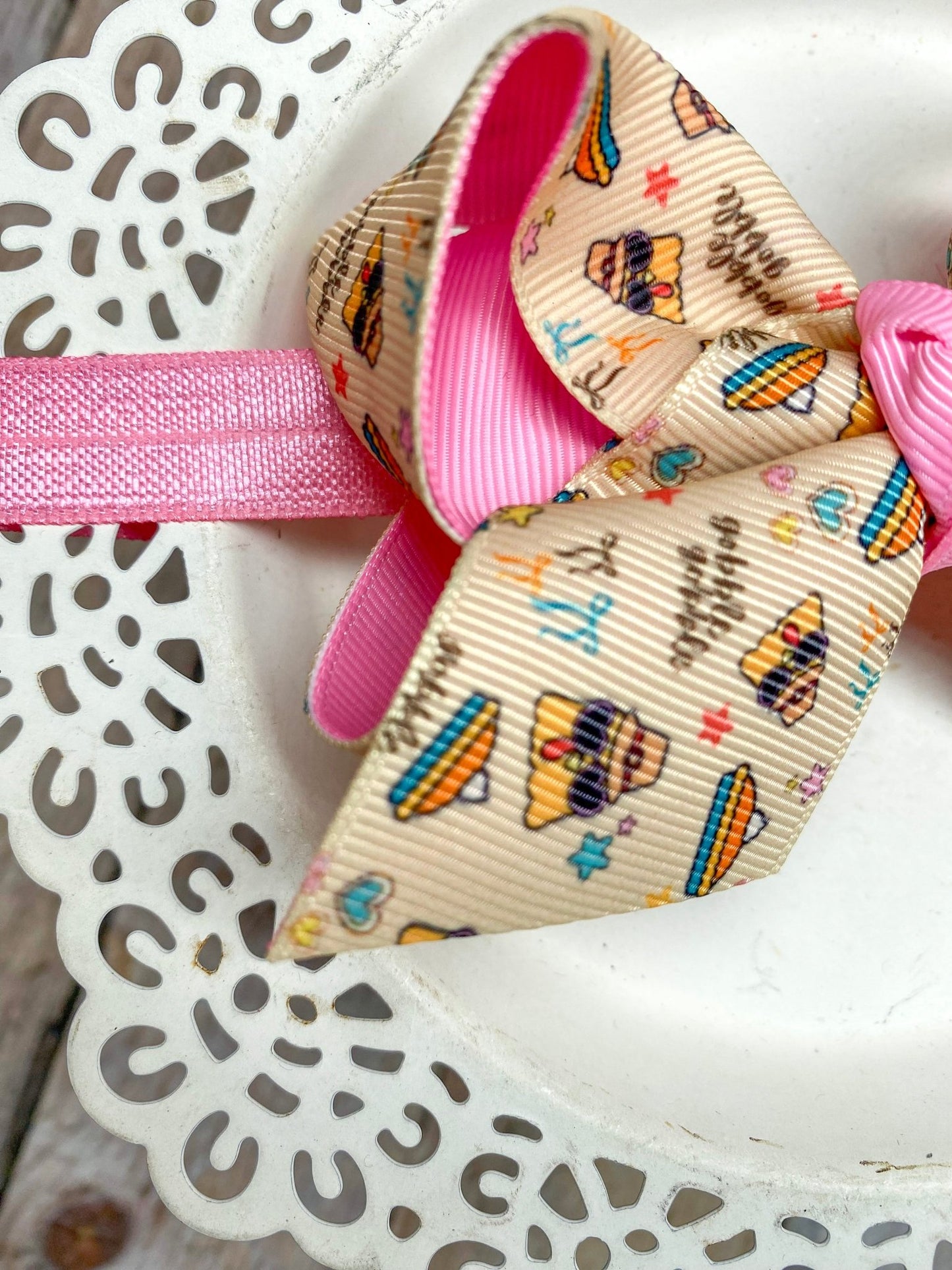 Close-up of a decorative bow with pink ribbon and patterned center on a white lace background