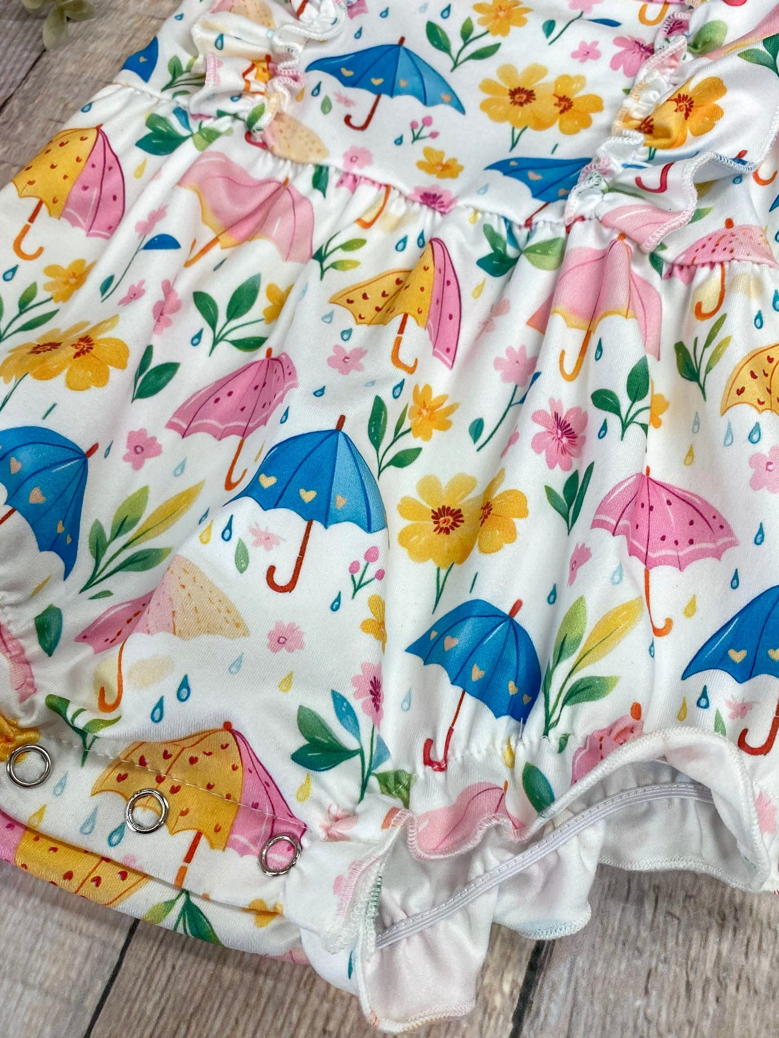 Baby romper with colorful umbrella and flower pattern on a wooden surface