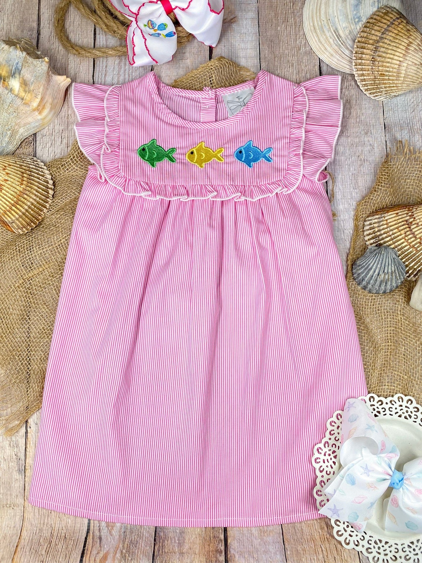 Pink dress with colorful fish appliqués on a wooden background