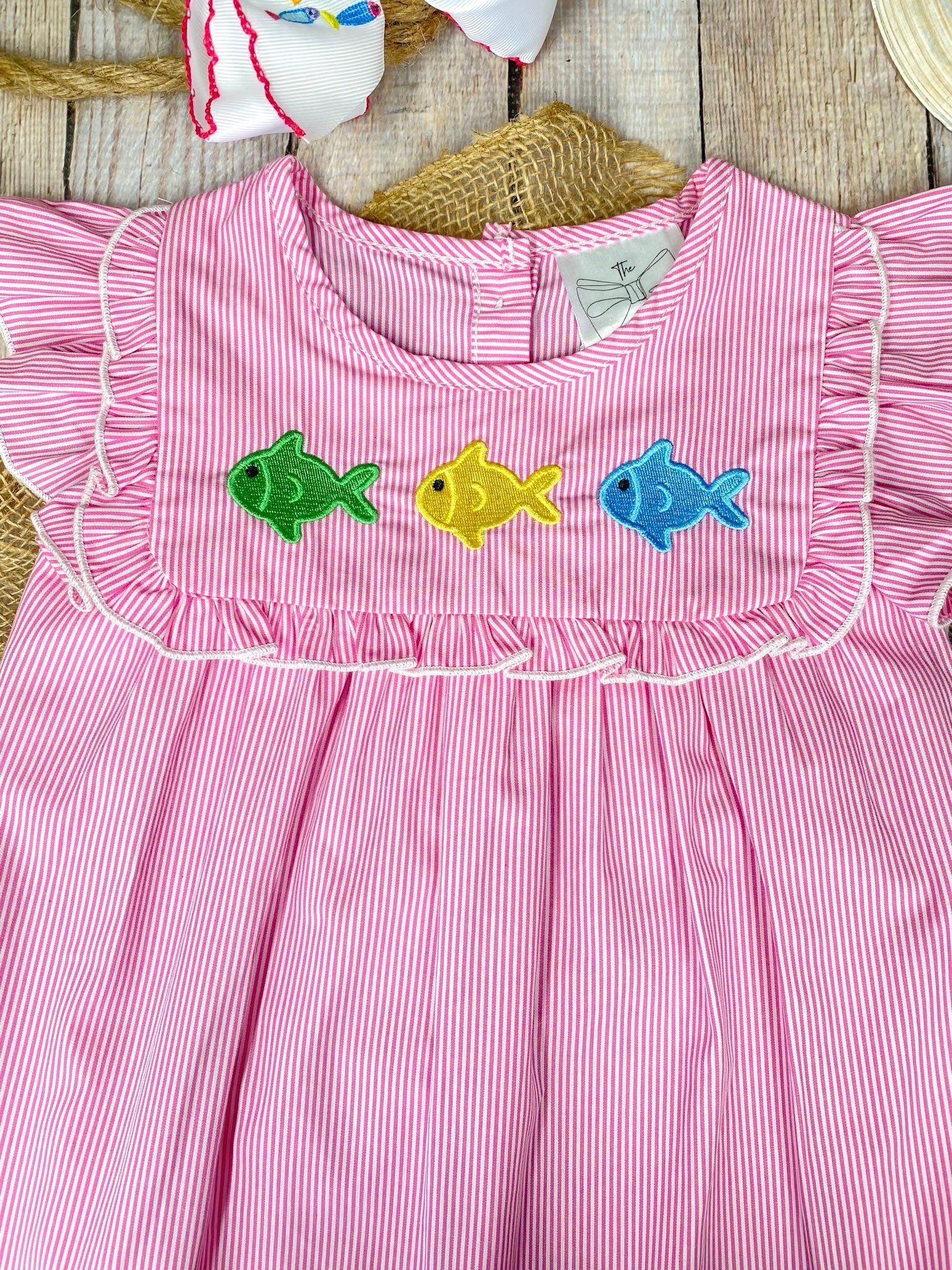 Pink dress with colorful fish appliqués on a wooden background