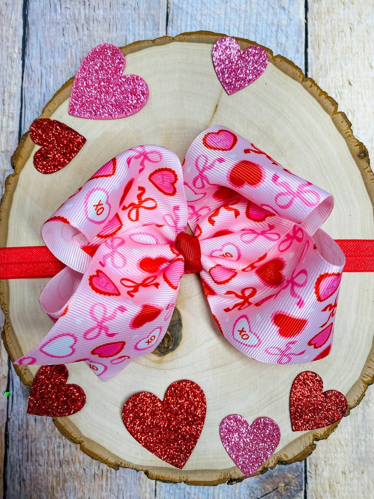 Pink hair bow with heart patterns on a wooden surface with glittery hearts.