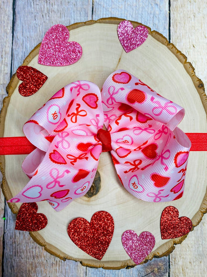 Pink hair bow with heart patterns on a wooden surface with glittery hearts.