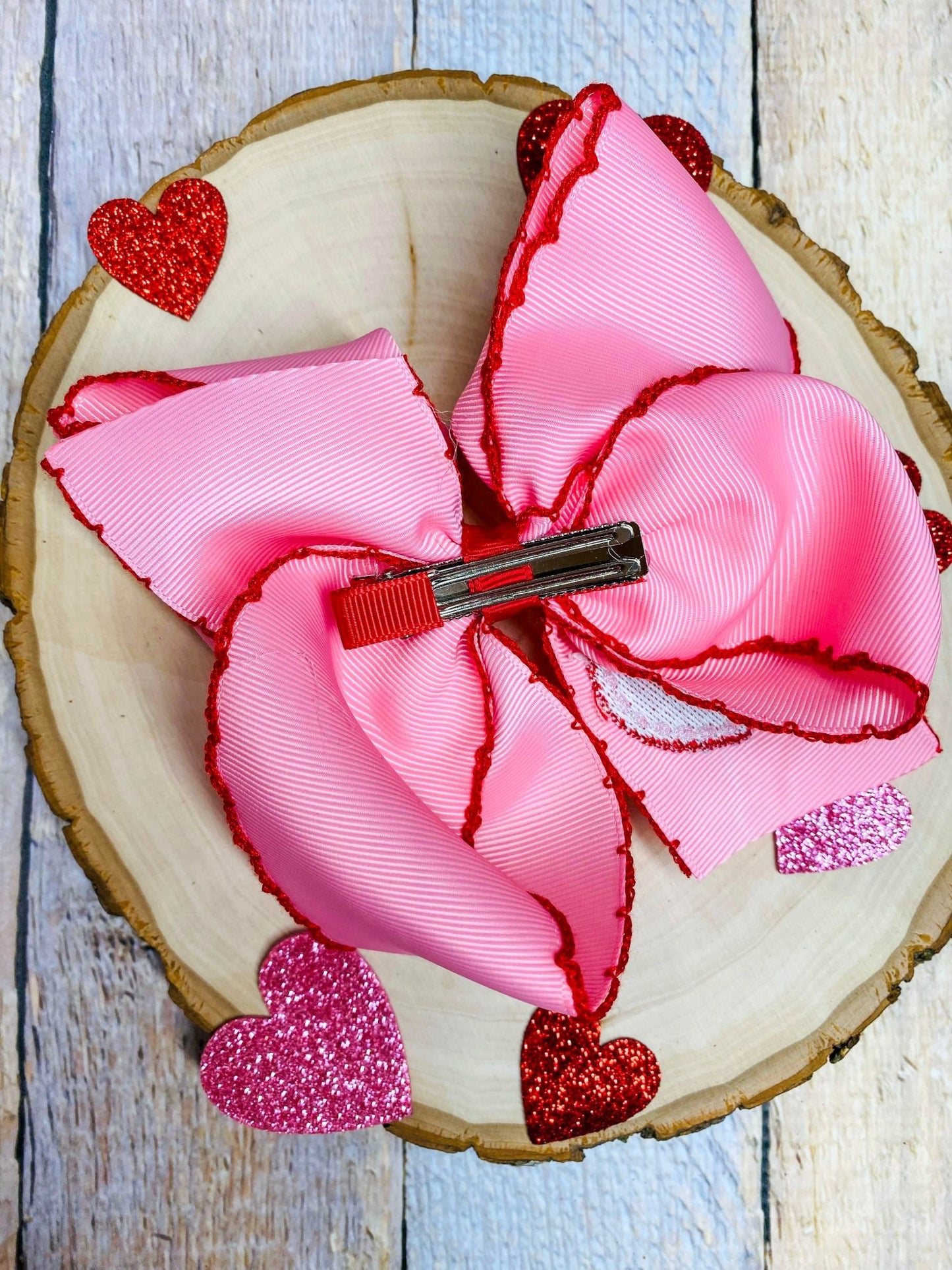 Pink hair bow with clip and red accents on a wooden surface