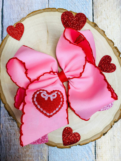 pink hair bows with red heart designs on a wooden surface.
