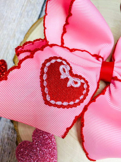 Pink and red heart-shaped ribbons with a central embroidered design on a wooden surface.