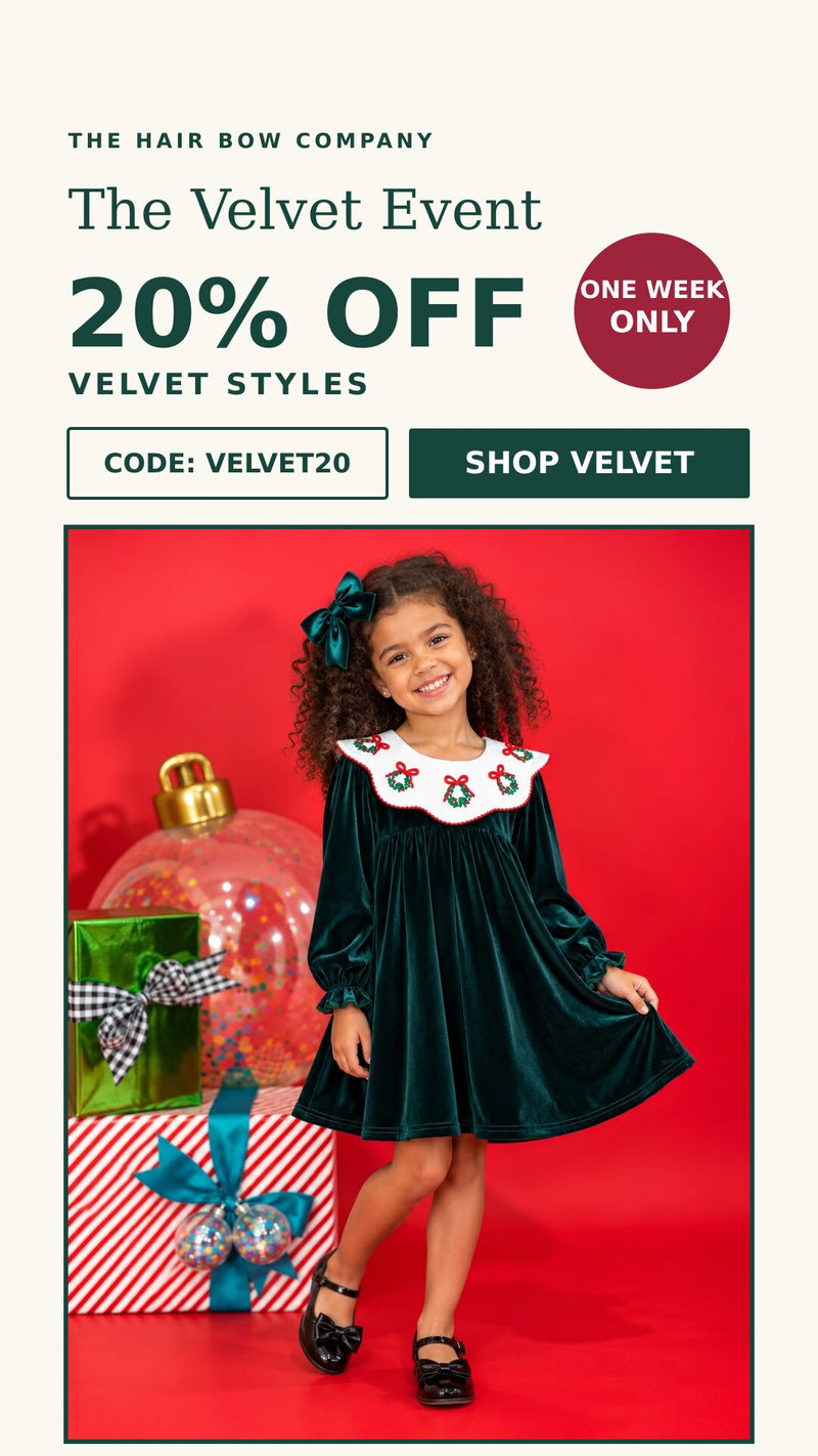 Smiling girl in a green velvet dress with a wreath collar and matching green bow. The Velvet Event: 20% off velvet styles with code VELVET20.