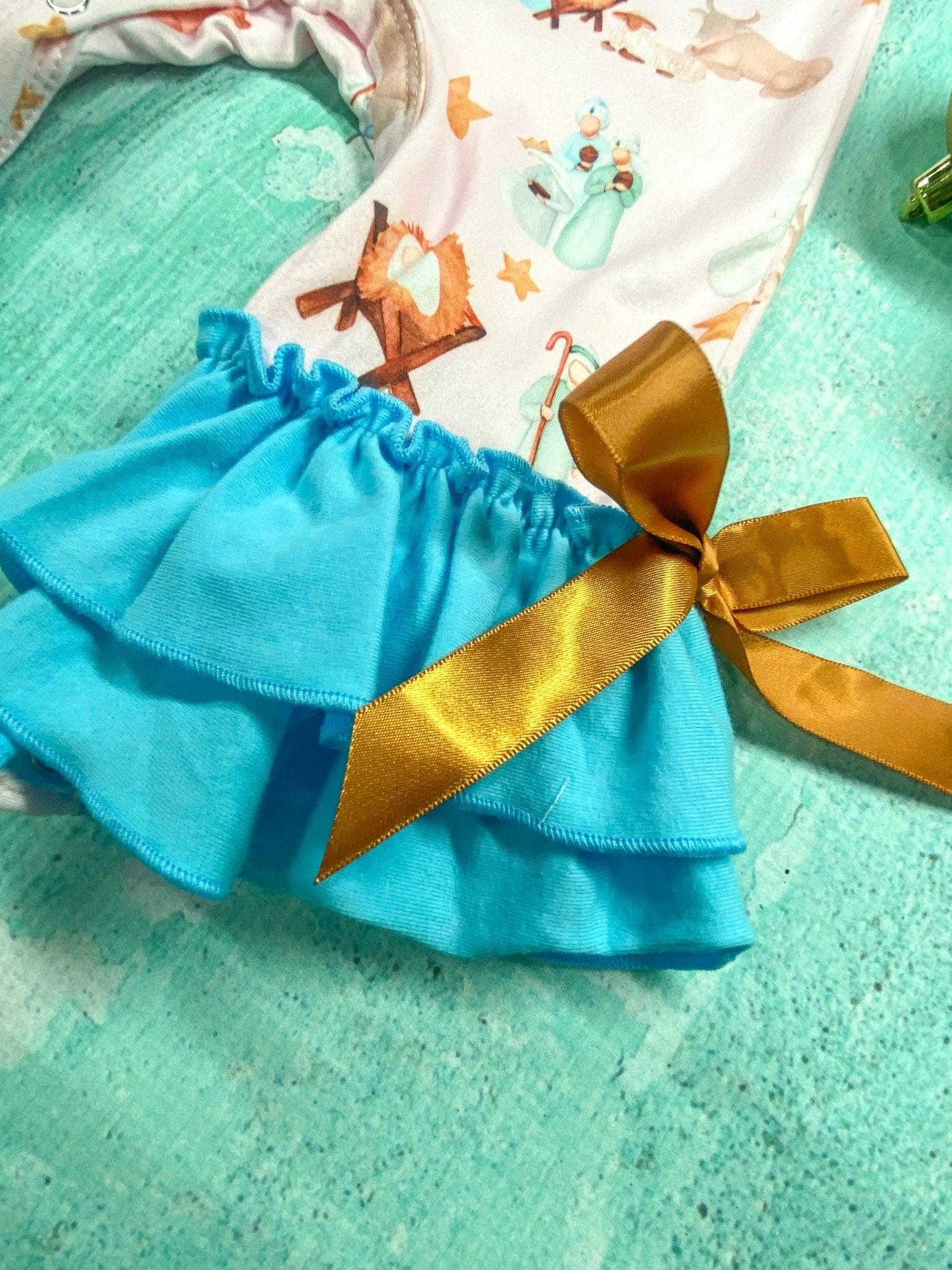 close up of a blue ruffles with a gold bow tied on the side at the end of the pant leg