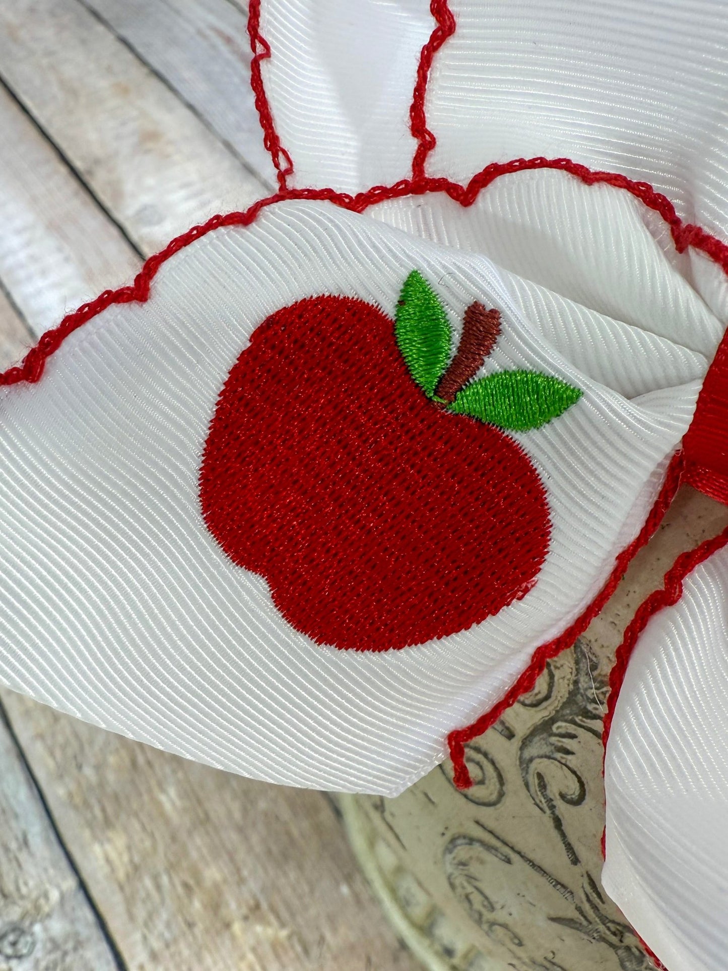 Close up of white apple embroidery on moonstitch bow headband