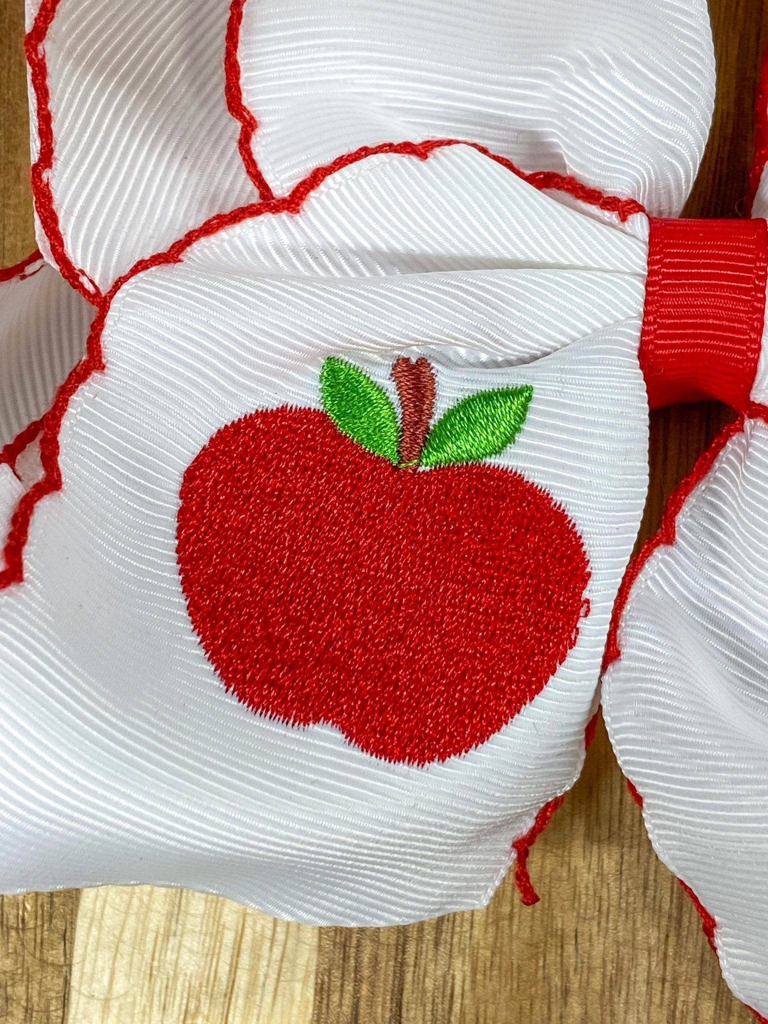 Close up of white apple embroidery on moonstitch hair bow