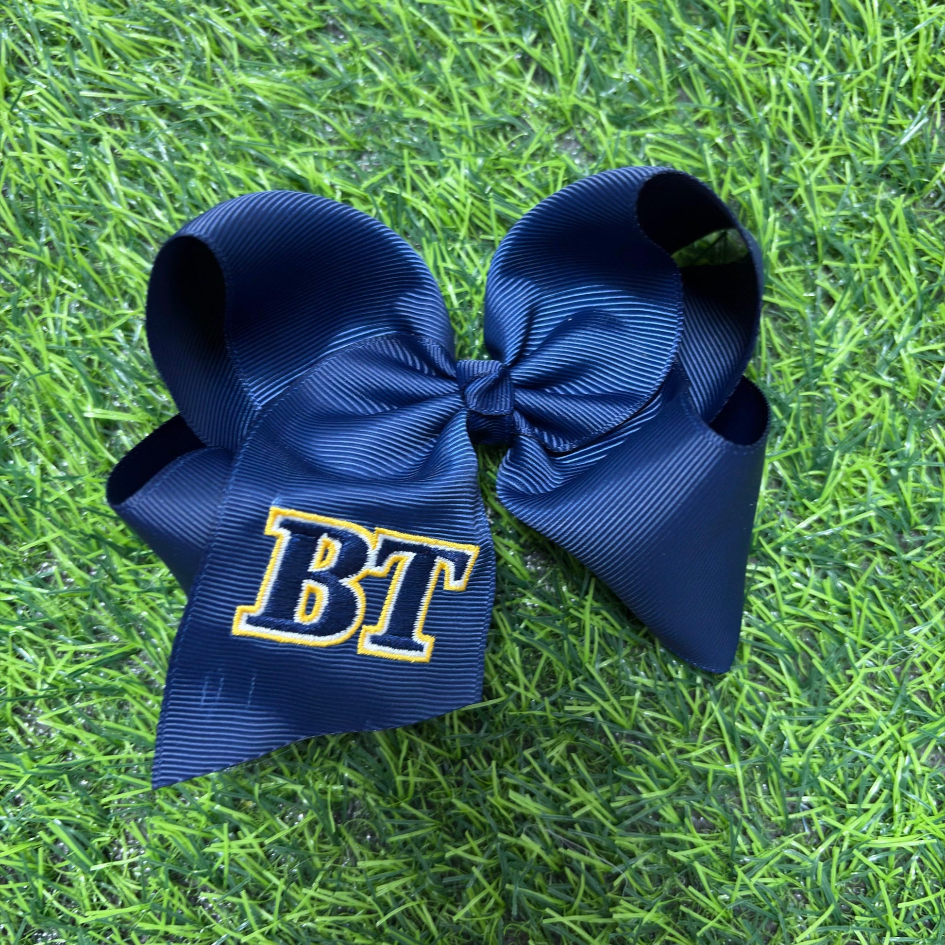 Two navy blue hair bows with 'BT' on a grass background